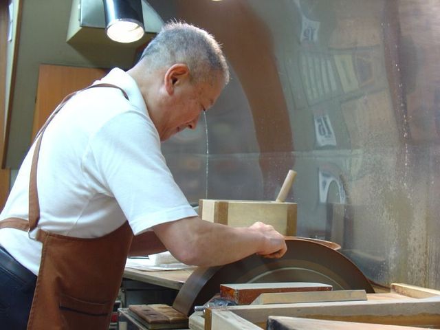 研磨機に包丁を当てて作業する職人の手元と、火花が出ている刃先
