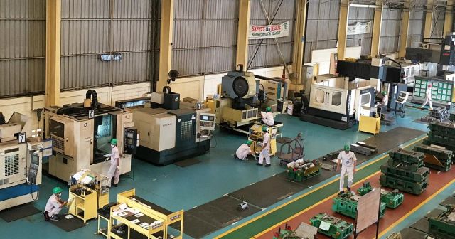 工作機械が並ぶ工場の通路と、機械の前で作業する作業者たち