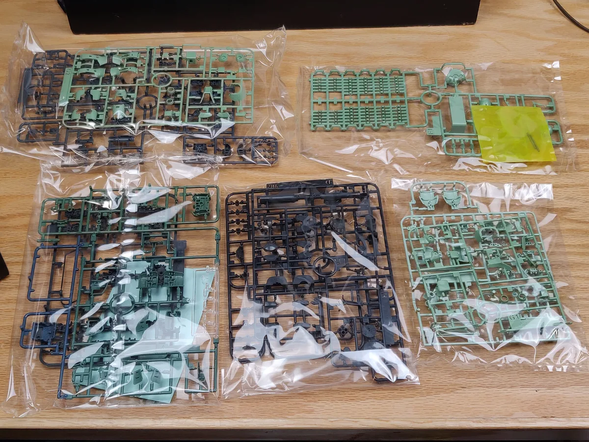 木の机に並べられた、緑色や灰色の枠につながるプラモデルの部品一式