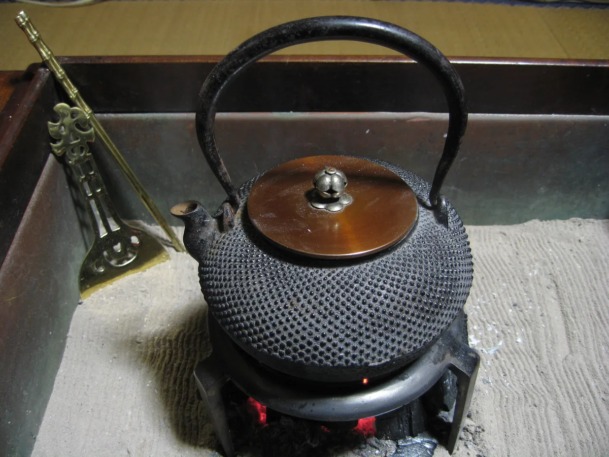 火鉢の上に置かれた、黒い本体と茶色のふたを持つ鉄瓶
